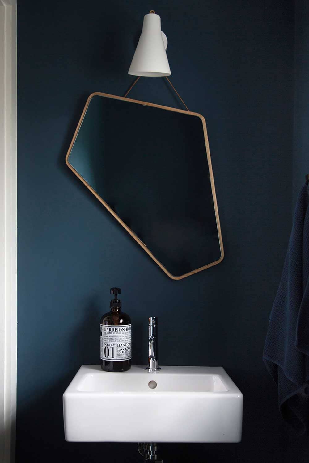 Lavabo blanc sublimé par un miroir design avec des murs bleu pétrole