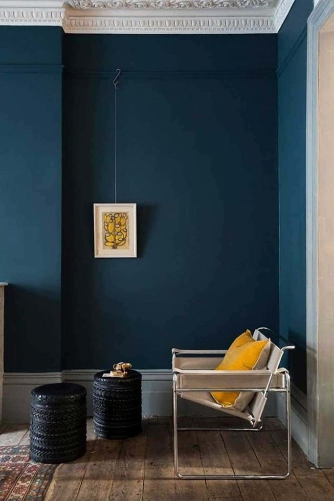 Salon de type Haussmannien avec murs bleu pétrole avec fauteuil jaune et parquet bois foncé